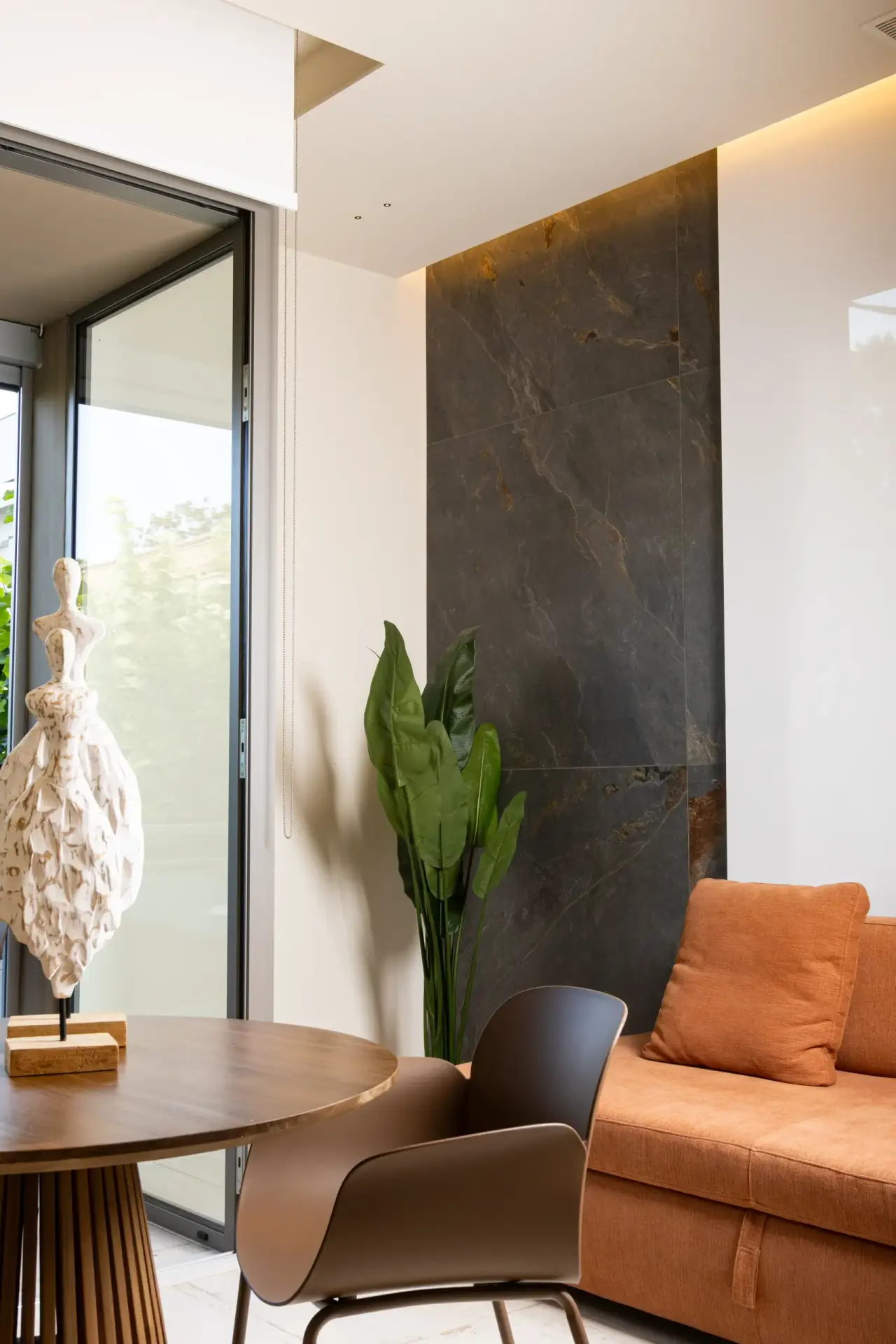 Angolo soggiorno con parete in gres effetto marmo, divano color terracotta e vetrata sul terrazzo