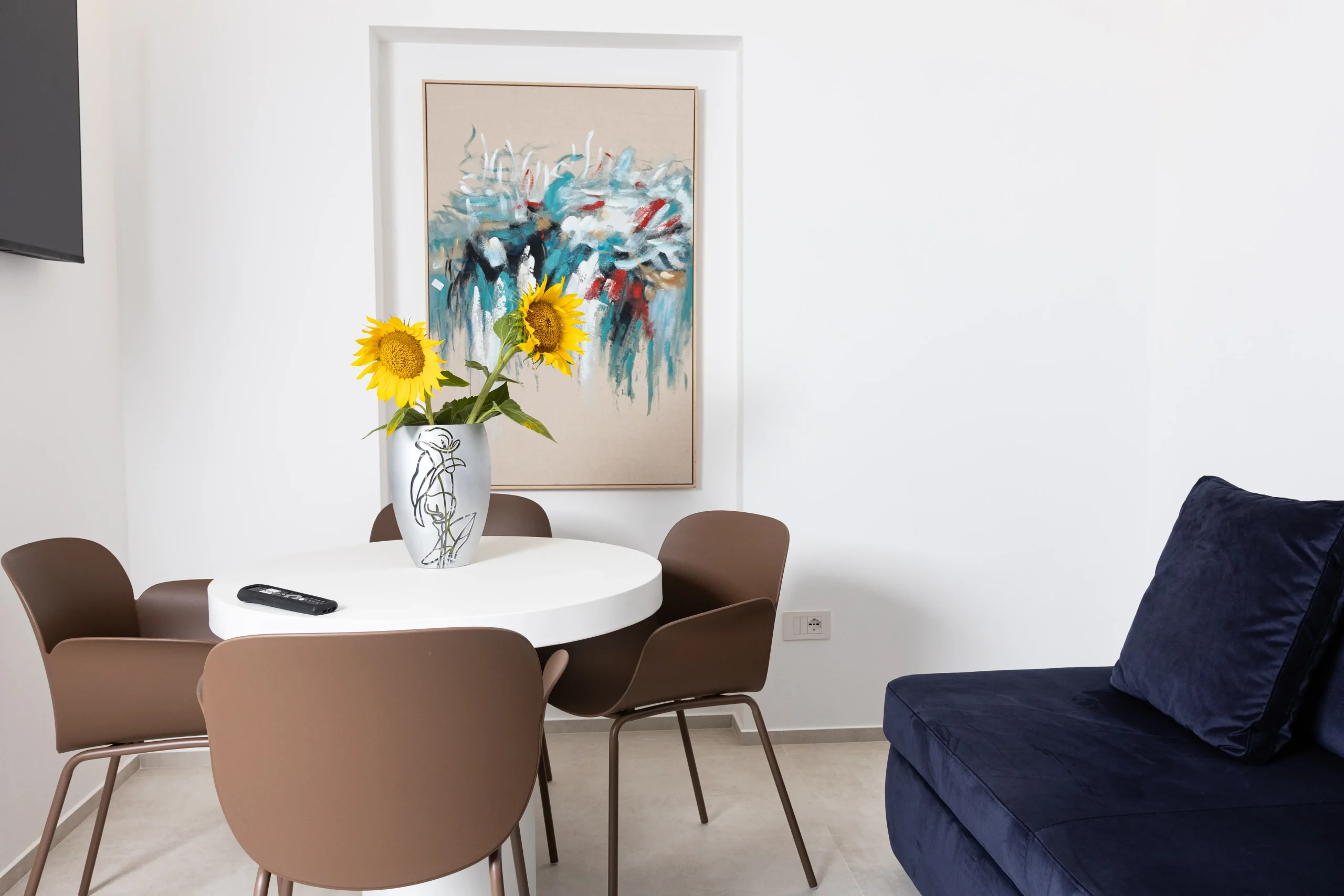 Tavolo rotondo con quattro sedie e girasoli, quadro astratto alla parete e divano blu