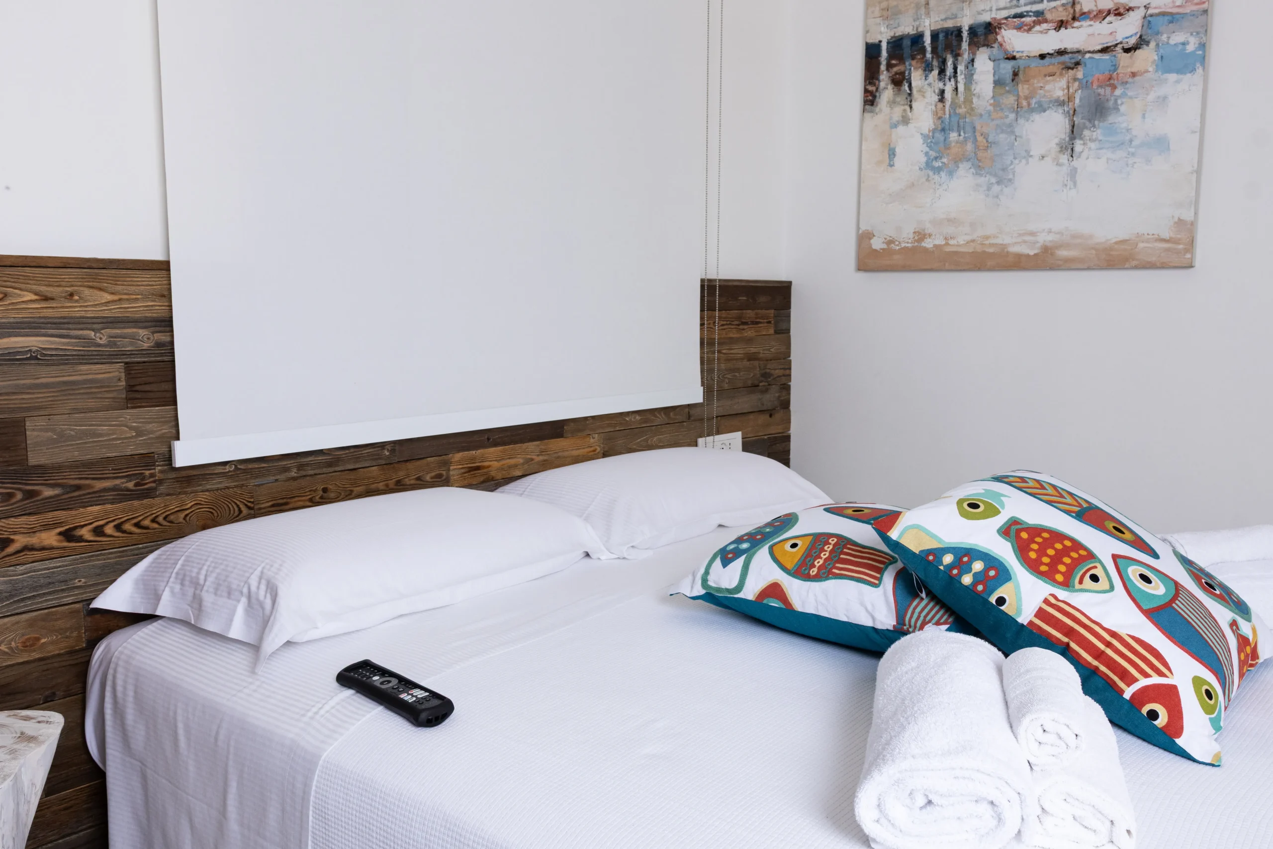 Letto matrimoniale con testiera in legno, cuscini con fantasia a pesci e asciugamani arrotolati