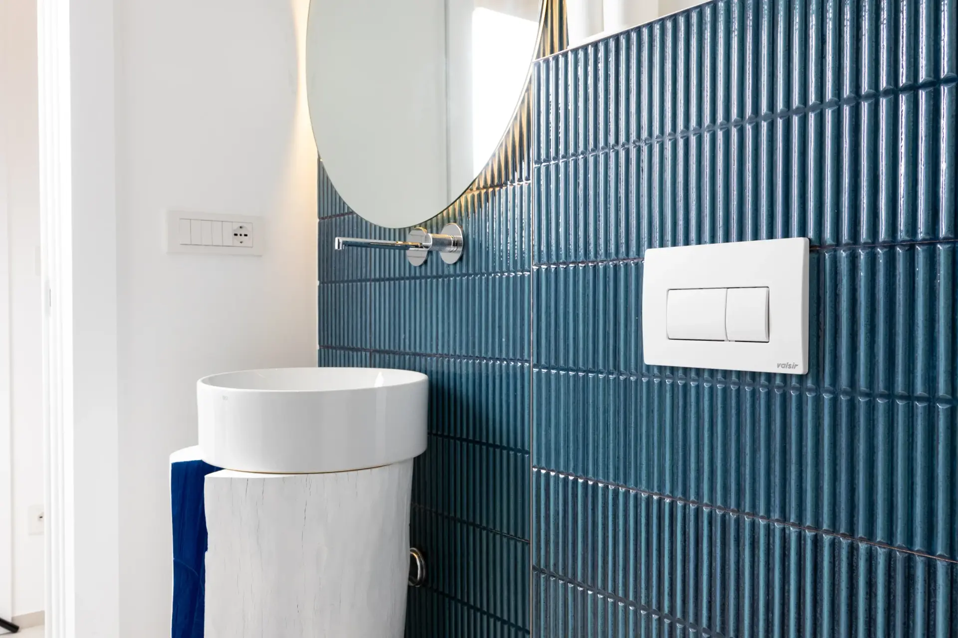 Bagno con rivestimento a scanalature blu, lavabo tondo su colonna in legno e specchio ovale