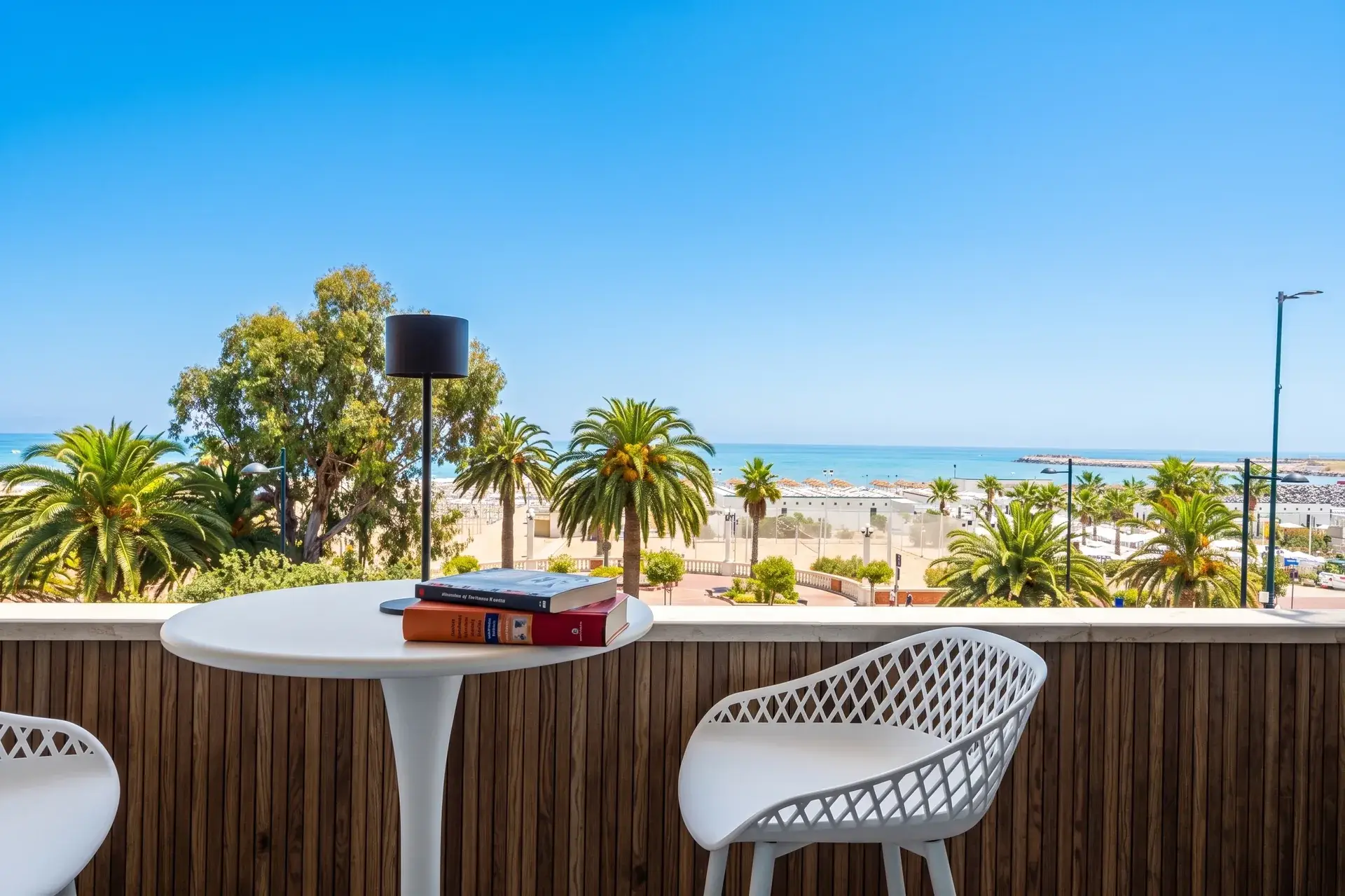 Tavolino e sedie sul balcone fronte mare, con palme e spiaggia di Giulianova sullo sfondo