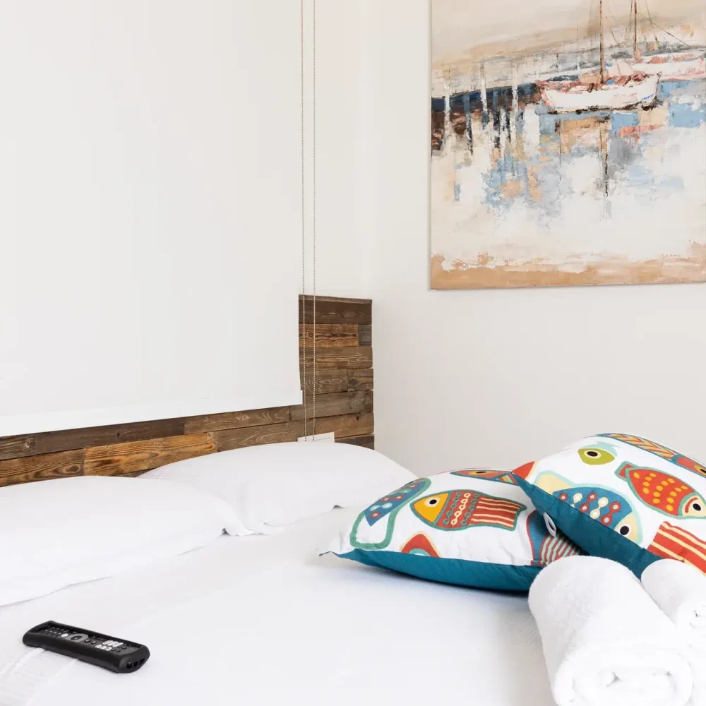 Camera matrimoniale con testata in legno di recupero, cuscini decorativi a pesci e quadro con barche