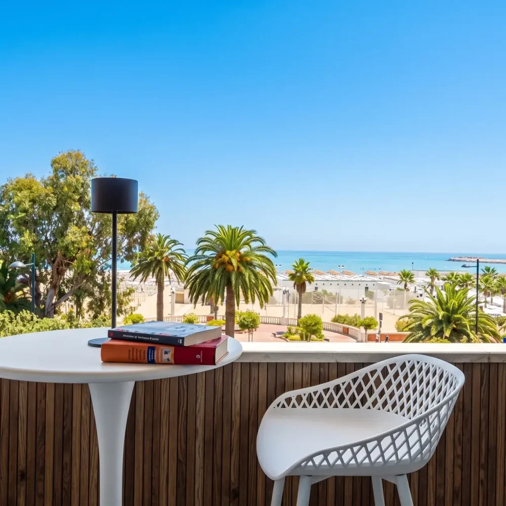 Tavolino e sedie sul balcone fronte mare, con palme e spiaggia di Giulianova sullo sfondo