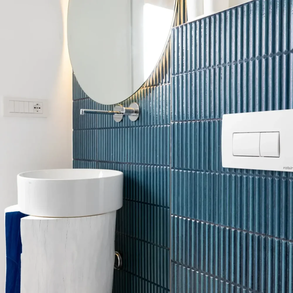 Bagno con rivestimento a scanalature blu, lavabo tondo su colonna in legno e specchio ovale